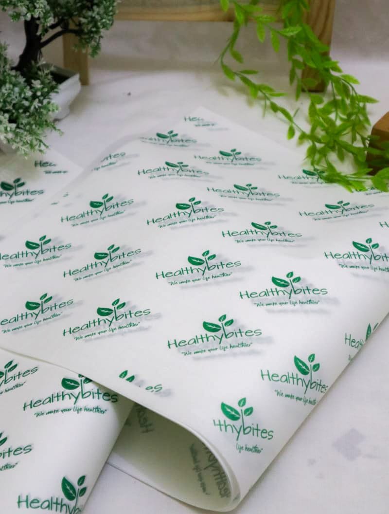 Sheet of adhesive labels featuring the Healthy Bites logo in green, with a tagline We make your life healthier. The sheet is placed on a surface with green plants in the background.